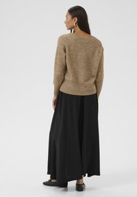 Pull en tricot marron avec un col rond, associé à une longue jupe noire. La tenue présente une coupe décontractée et une texture douce.