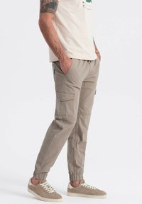 Beige cargobroeken met elastische boorden, zijzakken en een ontspannen pasvorm. Gepaard met beige sneakers en een lichtbeige shirt.