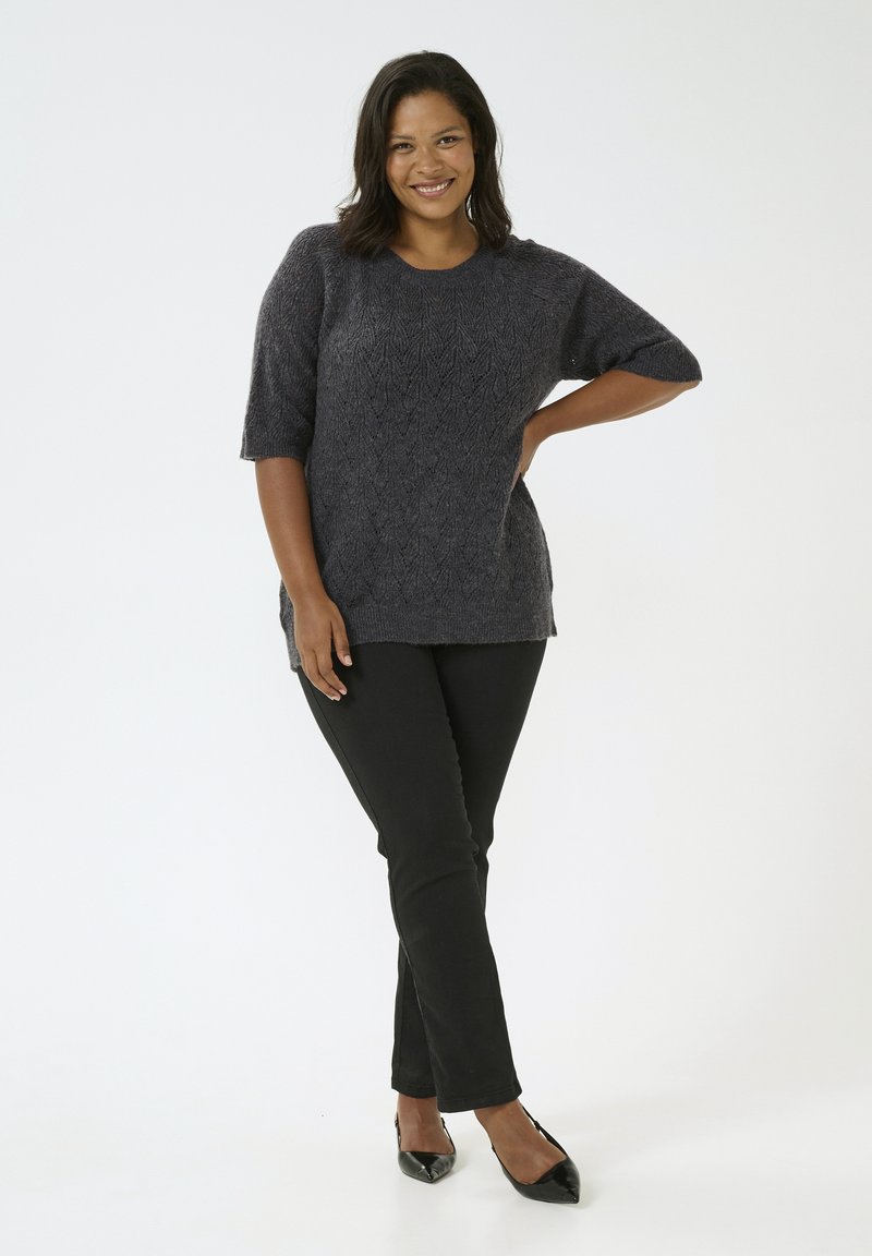 Ciemnoszary, krótki sweter dzianinowy z teksturowanym wzorem, zestawiony z gładkimi czarnymi spodniami i spiczastymi czarnymi szpilkami, stojący na jednolitym tle.