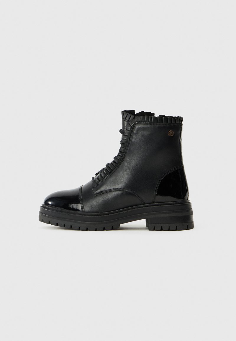 Botas negras hasta medio pantorrilla, hechas de cuero liso y charol, con un borde superior rizado y una suela gruesa texturizada con surcos.