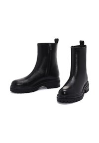 Botines de cuero negro con un acabado suave, cremallera lateral y suela de goma resistente. Presentan un tacón grueso y una pestaña trasera para facilitar su puesta.