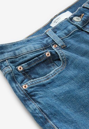 Úzké džíny ve středně modrém denimovém provedení, s měděnými nýty, malou kapsou a opotřebovaným okrajem detailu na kapse.