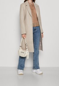 Světlý béžový kabát z vlněné směsi, hnědá košile na knoflíky, modré džíny, bílé tenisky a krémová taška se studovými akcenty.