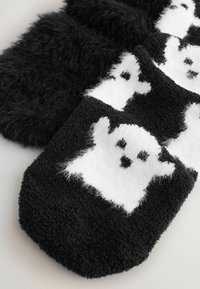 Black fuzzy socks with white ghost patterns alternating on the front, displayed on a light surface.