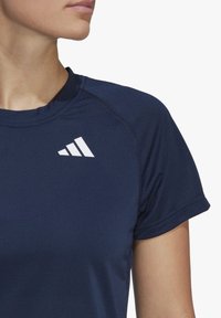 Marinblå atletisk t-shirt med kort ärm och rundad halsringning, tillverkad av strukturerad textil med en vit snedställd randig logotyp på bröstet.