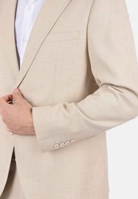 Blazer beige chiaro in tessuto testurizzato; presenta una tasca a bavero, rever a punta e cinque bottoni decorativi sui polsini.