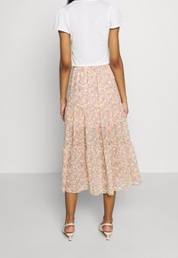 Jupe midi florale en rose clair avec des fleurs multicolores ; design à volants et tissu fluide ; associée à un top court blanc et des chaussures légères.
