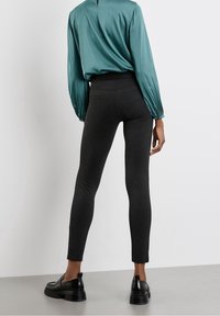 Mörkgrå leggings med en åtsittande design, tillverkade av stretchmaterial, i kombination med en tealblus med plisserade ärmar och en nyckelhålsklippning bak.