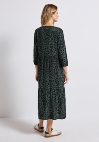 Grön leopardmönstrad klänning med trekvarts ärmar, lagerdesign och mjuk tyg. Buren med avslappnade sneakers som visar underbenet.