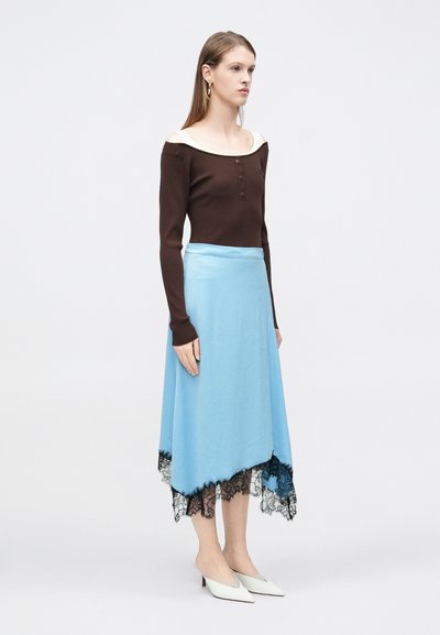 Καφέ μακρυμάνικη μπλούζα με ραβδώσεις και φαρδιά κρεμ λαιμόκοψη, συνδυασμένη με φούστα ανοιχτού μπλε χρώματος με μαύρη δαντέλα στο τελείωμα, φορεμένη με λευκές μπαλαρίνες.