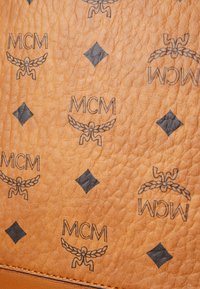 Surface en cuir tan présentant un motif répétitif de logos noirs et d'accents en forme de diamant, avec une finition texturée et un grain visible.