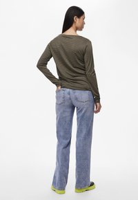 Langermet, olivengrønn ribbestrikket skjorte parret med lyseblå, utsvingte jeans og svarte sko med limegrønne såler, sett fra baksiden.