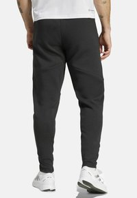 Sorte sweatpants med en tapered design, fremstillet af et tekstureret stof og subtile paneldetaljer. Båret med hvide træningssko.