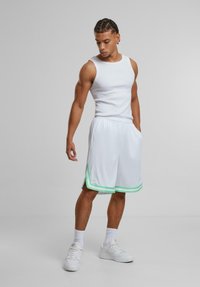 Shorts de sport blancs avec des bandes accentuées vertes, un débardeur blanc et des baskets blanches. Le tissu semble léger et lisse.