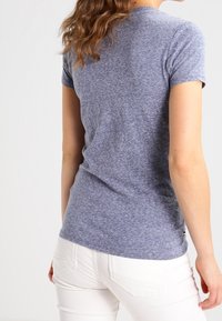 Kortärmad blå melerad t-shirt med rund halsringning, tillverkad av mjukt tyg, kombinerad med vita denimjeans. Enkel design; inga framträdande detaljer.