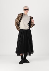 Casaco de estampa de leopardo, suéter de malha cinza com aplicações, saia preta de renda maxi e sapatos pretos robustos, usados com óculos de sol escuros.