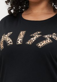 Μαύρο μπλουζάκι με μεγάλη, λεοπάρ εκτύπωση στις γράμματα που έχουν μεταλλικά στοιχεία και γράφει "KIZ." Μαλακό βαμβακερό ύφα σμα με στρογγυλή λαιμόκοψη.