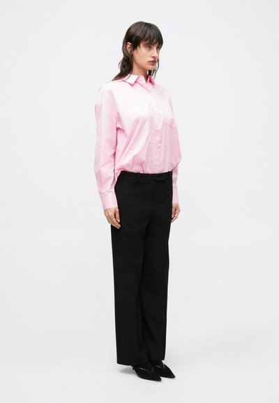Svetloružová košeľa na zapínanie s golierom, kombinovaná s elegantnými čiernymi nohavicami a špicatými čiernymi topánkami. Hladká tkanina s voľným strihom.