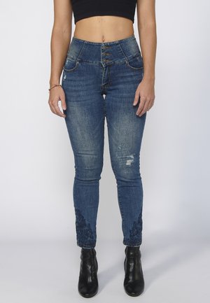 High-waisted denim jeans in a faded blue with five-button closure, distressed details, and lace embroidery at the hems.