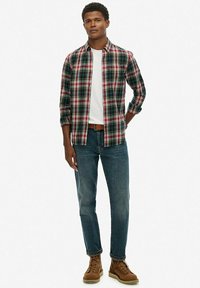 Camisa de franela a cuadros en verde, rojo y blanco; combinada con una camiseta blanca sencilla, jeans azules y botas marrones de cordones.