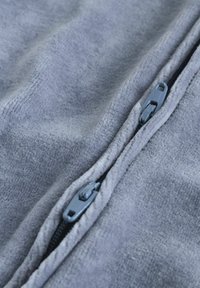Grå fleece stof med en blød tekstur, der har en sort lynlås og en grå lynlåsholder, der fremhæver glatte linjer langs sømmen.