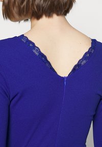 Top roxo com decote em V e rendas na parte de trás, além de um pequeno fecho de zíper. Tecido suave com um design ajustado.