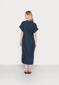 Vestido de linho azul-marinho com mangas curtas, um corte solto e fendas laterais, apresentando um design simples nas costas e sem hardware visível.