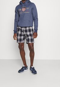 Sudadera azul marino con logo, pantalones cortos de cuadros en blanco y negro, y zapatillas azul marino. Presenta un bolsillo tipo canguro y cintura con cordón.