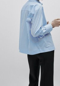 Camicia a righe blu e bianche con vestibilità rilassata, polsini con bottoni e orlo curvo, abbinata a pantaloni neri. Tessuto in cotone morbido.