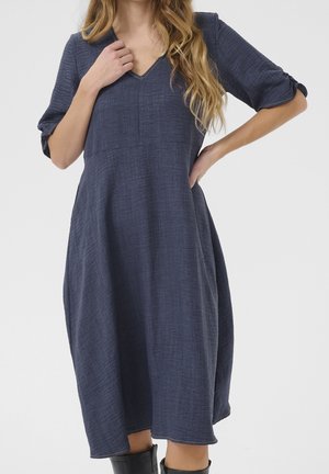 Robe bleu marine en tissu texturé avec un col en V et des manches trois-quarts, dotée d'une jupe évasée et de coutures apparentes.