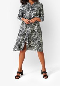 Abito a motivi paisley in bianco e nero con colletto, maniche a tre quarti e spacco frontale. Indossato con sandali neri a tacco grosso.