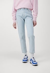 Jeans de mezclilla azul claro con corte recto, combinados con zapatillas azules y blancas y una sudadera rosa, que exhiben un look casual.