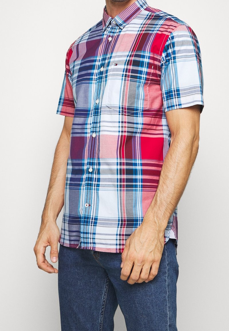Camicia a maniche corte a quadri con un mix di colori rosso, blu e grigio, chiusura con bottoni e dettaglio tasca. Realizzata in tessuto leggero.