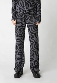 Schwarz gemustertes Set mit langärmeliger Bluse und weit geschnittenen Hosen. Strukturierter grauer Blumenprint auf dem Stoff. Stilisiert mit klobigen schwarzen Schuhen.