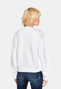 Sweatshirt blanc avec des manches longues et larges et des poignets côtelés. Texture lisse, taille ajustée et un design simple et épuré.