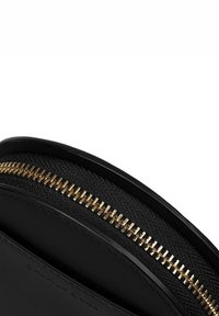 Borsetta rotonda nera con un esterno in pelle liscia e una parte superiore in tessuto texturizzato. Presenta una zip in metallo dorato che corre lungo il bordo superiore.