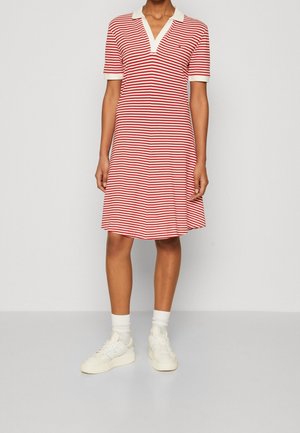Personne portant une robe à manches courtes rayée horizontale rouge et blanche jusqu'aux genoux, avec un col blanc, des chaussettes blanches et des baskets blanches.