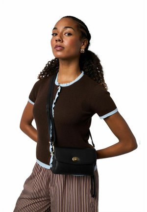 Bolso cruzado de cuero negro con herrajes dorados, textura suave y cierre de solapa; llevado sobre una camiseta marrón de canalé con ribete azul claro.