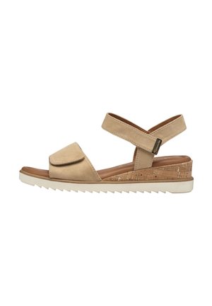 Beige sandal med åben tå og ankelrem, kork kilehæl og hvid rillede sål, vist fra siden på en hvid baggrund.