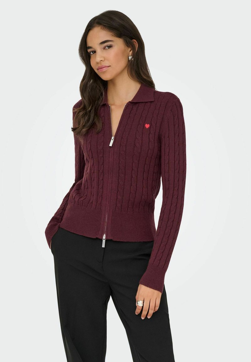 Burgundijas krāsas zip-up kardigāns ar kabelīšu adījumu, ar sarkanu sirds detaļu kreisajā krūtīm un ribu aprocēm un apakšmalu.