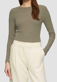 Top de manga larga de color verde oliva con textura acanalada, combinado con pantalones de tiro alto de color crema que cuentan con pliegues frontales y bolsillos laterales.