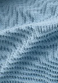 Tissu texturé bleu clair avec un petit motif en grille, présentant un tissage doux et respirant, adapté pour les vêtements ou les textiles d'intérieur.