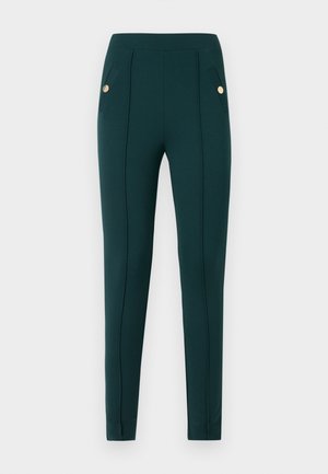 Pantalon vert foncé ajusté avec coutures frontales et rabats de poche boutonnés, présenté sur un fond clair uni.