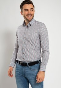Kleurige button-up shirt met een geometrisch patroon in rood, groen en blauw, met een klassieke kraag en lange mouwen. Draagt met blauwe jeans.