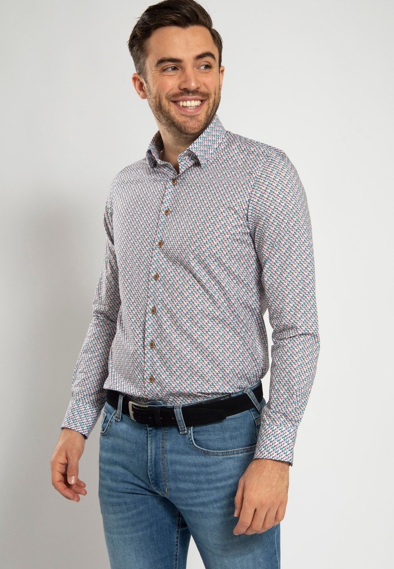 Kleurige button-up shirt met een geometrisch patroon in rood, groen en blauw, met een klassieke kraag en lange mouwen. Draagt met blauwe jeans.