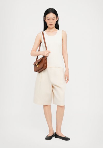 Beige ermeløs topp, kremfargede knelange shorts, svarte leiligheter, og en brun crossover-veske med gullfarget detaljer. Glatt stoff og skreddersydd design.