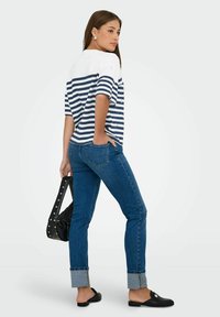 Blouse à manches courtes, blanche et rayée bleu marine, associée à un jean bleu avec des ourlets roulés et des chaussures noires à enfiler. Sac noir pendu à la main.