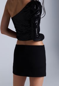 Czarny top z cekinami na jedno ramię, z marszczonym rękawem; w połączeniu z dopasowaną, czarną mini spódnicą. Gładka faktura, błyszczące akcenty.