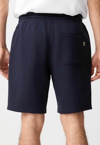 Bermudas de algodón azul marino con una cintura elástica, dobladillo recto y un único bolsillo trasero que presenta una discreta etiqueta de marca. Textura suave.