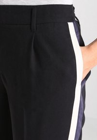 Black pants with a smooth texture, featuring a contrasting white side stripe. Includes a pocket at the hip and a flat waistband.
